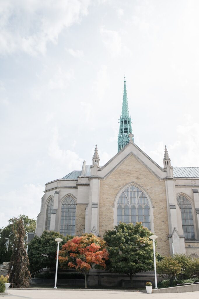 Exterior view of a historic Detroit church featuring Gothic architecture, tall windows, and a prominent green spire rising above surrounding trees. The landmark ceremony location represents one of the timeless places to get married in Detroit MI, offering a classic setting for couples planning a traditional Detroit wedding. Detroit ceremony venue photographed by local photographer Courtney Rudicel.