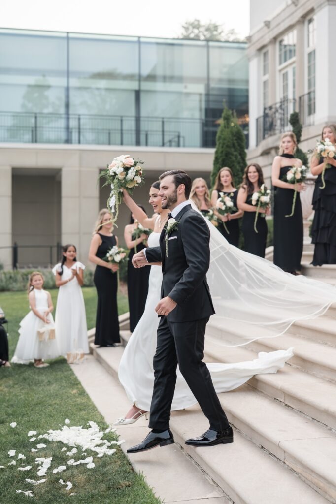 Bride and groom smiling as they walk down the steps after their outdoor wedding ceremony beside Lake St. Clair.