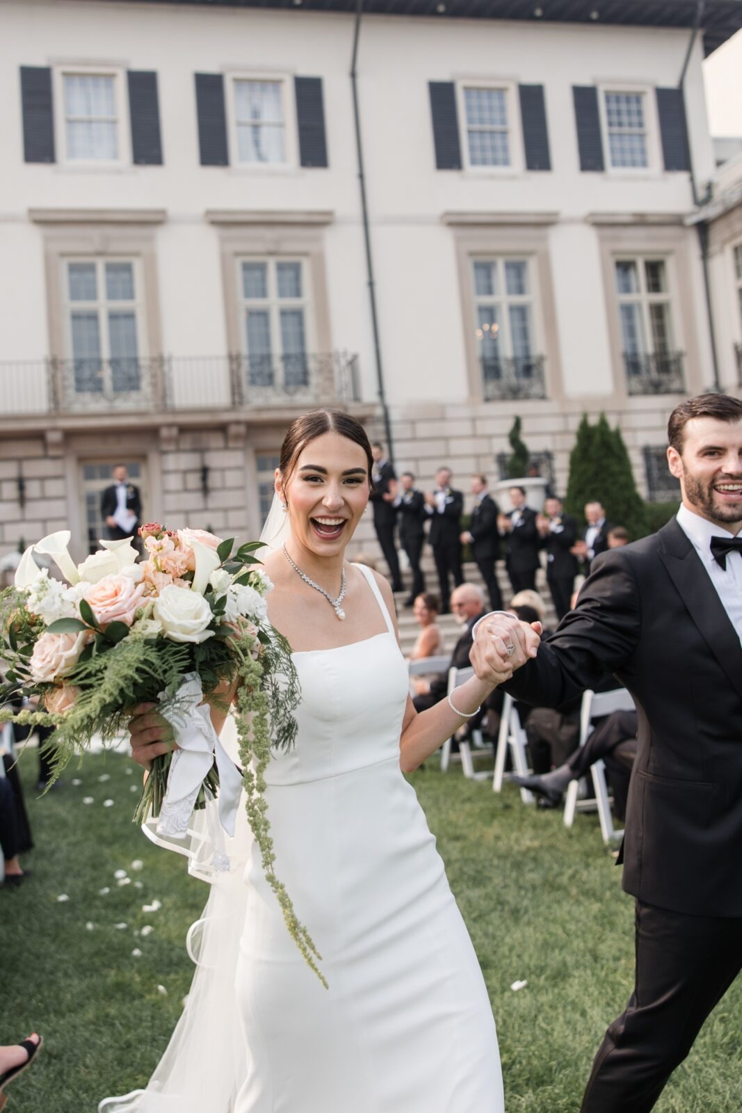 Bride and groom smiling and holding hands as they walk back up the aisle together after their outdoor wedding ceremony.